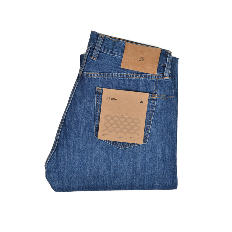 Folded blue jeans with a brown label on a white background. 3sixteen Classic Straight 101X Selvedge Stonewash