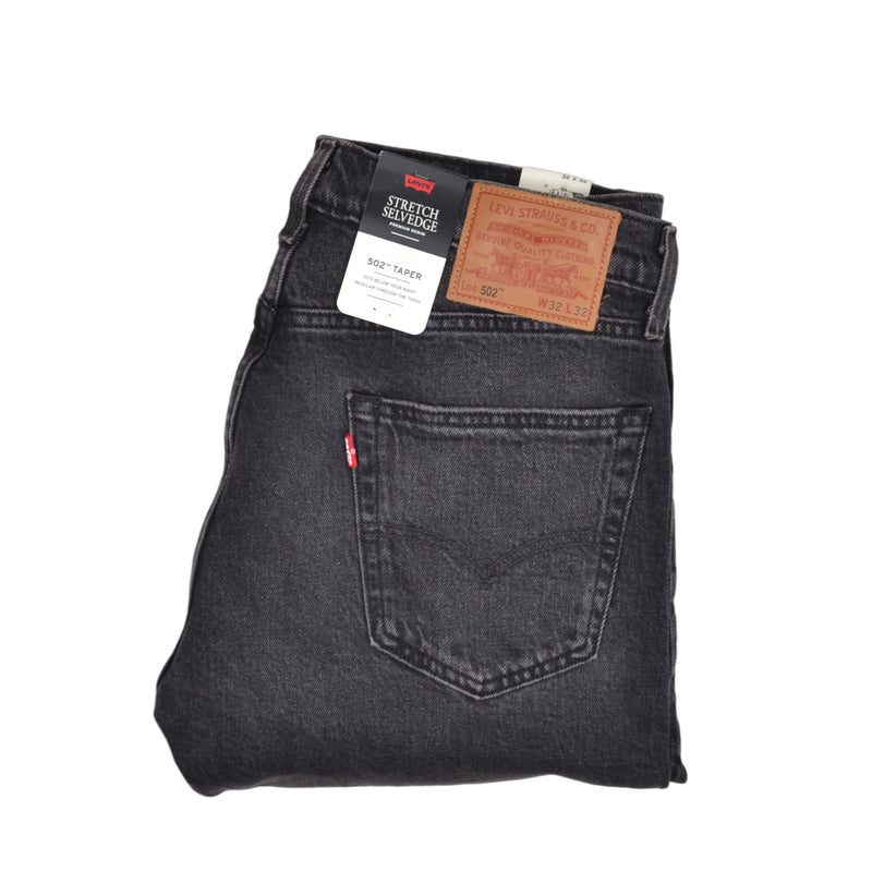A folded pair of Levi's Straight Denim jeans in a washed black finish, showing the back pocket with the signature red tab and attached leather patches, set against a plain white background.