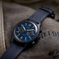 A Timex wristwatch with a dark blue leather strap and a dark blue dial, resting on a textured brown canvas surface.
