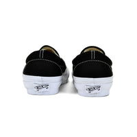 Black slip-on sneakers with white soles on a white background